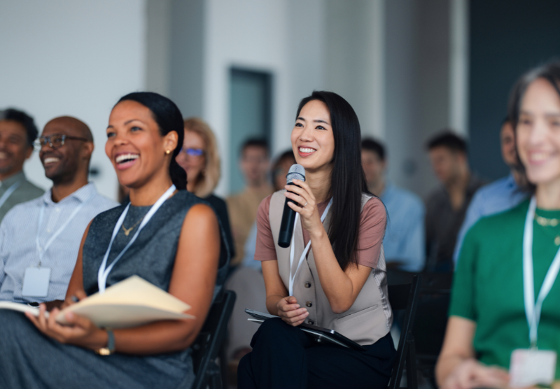 Diverse group of individuals in a meeting with a woman holding a microphone